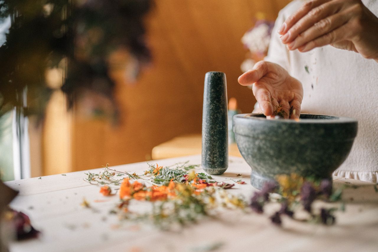 Close-up of hands preparing herbal medicine with a mortar and pestle on a table.